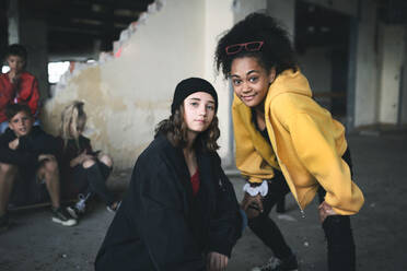 Front view of group of teenagers girl gang standing indoors in abandoned building, hanging out. - HPIF13628