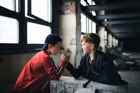 Side view of teenagers boys indoors in abandoned building, arm wrestling. - HPIF13634