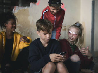 Vorderansicht einer Gruppe Jugendlicher, die in einem verlassenen Gebäude sitzen und Smartphones benutzen. - HPIF13665