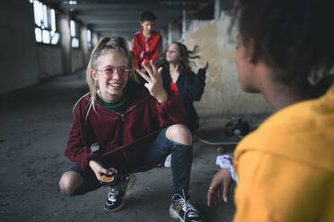 Front view of group of teenagers gang sitting indoors in abandoned building, using smartphones. - HPIF13666