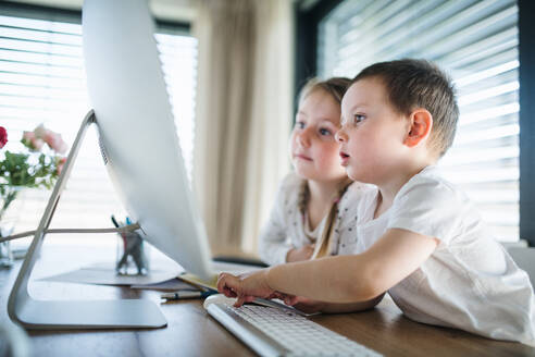 Kleines Mädchen und Junge sitzen am Tisch und benutzen den Computer zu Hause. Corona-Virus und Quarantäne-Konzept. - HPIF13720