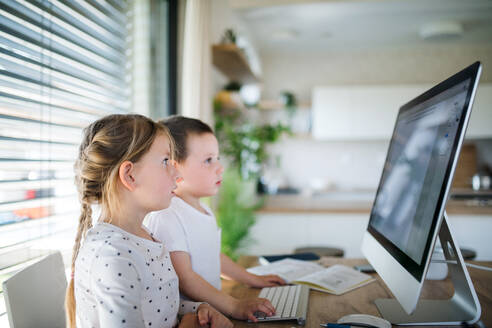 Kleines Mädchen und Junge sitzen am Tisch und benutzen den Computer zu Hause. Corona-Virus und Quarantäne-Konzept. - HPIF13721