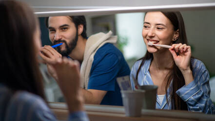 Porträt eines jungen Paares beim Zähneputzen vor einem Spiegel zu Hause. - HPIF13767
