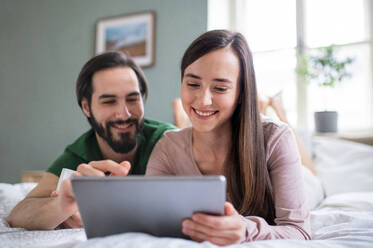 Happy young couple in love using tablet on bed indoors at home. - HPIF13780