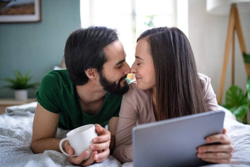 Glückliches, verliebtes junges Paar, das auf dem Bett zu Hause ein Tablet benutzt. - HPIF13782