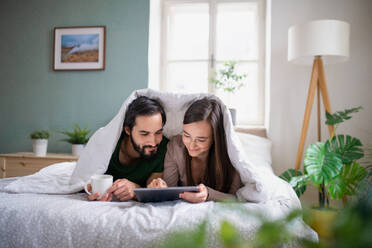 Glückliches, verliebtes junges Paar, das auf dem Bett zu Hause ein Tablet benutzt. - HPIF13785