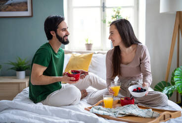 Glückliches, verliebtes junges Paar frühstückt zu Hause auf dem Bett und unterhält sich. - HPIF13789