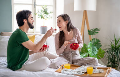 Glückliches, verliebtes junges Paar beim Frühstück auf dem Bett zu Hause. - HPIF13791