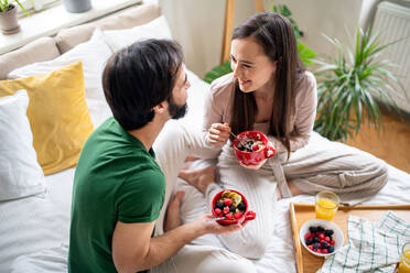 Happy young couple in love eating breakfast on bed indoors at home. - HPIF13795