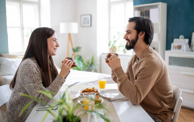 Happy young couple in love eating hamburgers indoors at home. - HPIF13796