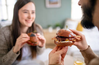 Glückliches, unerkanntes, verliebtes Paar, das drinnen zu Hause Hamburger isst. - HPIF13797