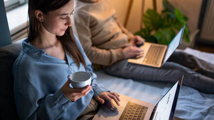Unbekanntes junges Paar mit Laptops auf dem Bett im Haus, Home-Office im Sperrkonzept. - HPIF13803