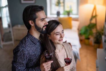 Happy young couple in love holding glasses of wine indoors at home. - HPIF13805