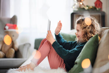 Kleines Mädchen mit Tablet, das zu Weihnachten zu Hause sitzt und einen Videoanruf führt. - HPIF13831