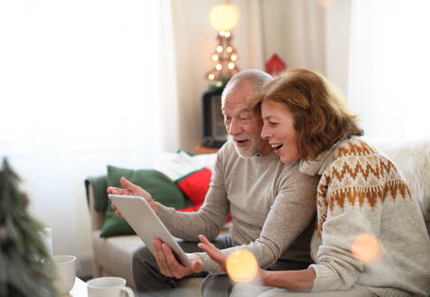 Seitenansicht eines glücklichen älteren Paares zu Hause an Weihnachten, das einen Videoanruf mit der Familie führt. - HPIF13840