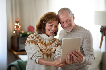 Lächelndes älteres Paar hält festliche Erinnerungen mit einem Tablet fest und posiert für ein fröhliches Weihnachts-Selfie zu Hause - HPIF13847