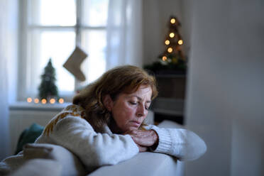 Portrait of lonely senior woman sitting and sleeping on sofa indoors at Christmas, solitude concept. - HPIF13857