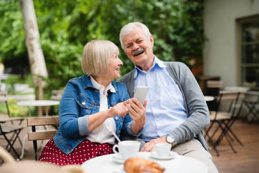 Portrait of happy senior couple in love sitting outdoors in cafe, using smartphone. - HPIF13866