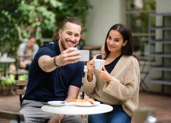Ein fröhliches Paar hält einen Moment seiner Liebe und seines Glücks fest, während es einen Kaffee in einem Café im Freien genießt - HPIF13871