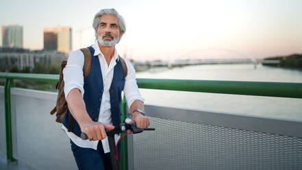 Portrait of mature man commuter with electric scooter outdoors in city, going to work. Copy space. - HPIF13888