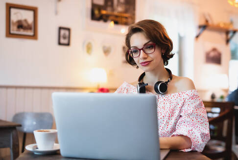 Porträt einer jungen Frau mit Kopfhörern und Laptop, die in einem Café arbeitet. - HPIF13892