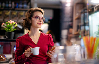 Porträt einer jungen Frau mit Kaffee in einem Café, die ihr Smartphone benutzt. - HPIF13894