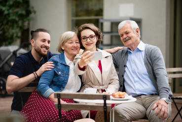 Happy senior couple with adult son and daughter sitting outdoors in cafe, taking selfie. - HPIF13908