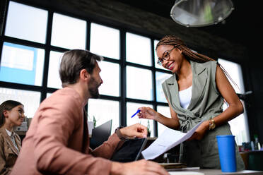 Low angle view portrait of young businesspeople working indoors in office, talking. - HPIF13918