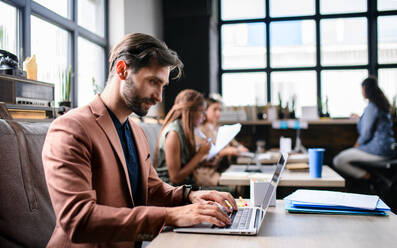 Portrait of young businesspeople with laptop sitting and working indoors in office. - HPIF13925