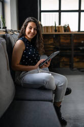 Porträt einer jungen Geschäftsfrau, die in einem Büro sitzt und in die Kamera schaut. - HPIF13936