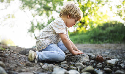 Seitenansicht eines glücklichen kleinen Jungen, der mit Steinen und Schlamm in der Natur spielt. - HPIF13963