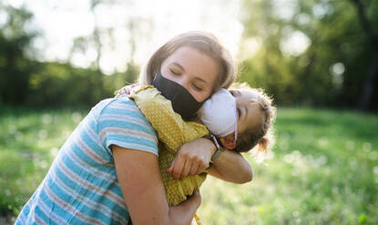 Side view of happy mother hugging small daughter on trip in nature, wearing face masks. - HPIF13967