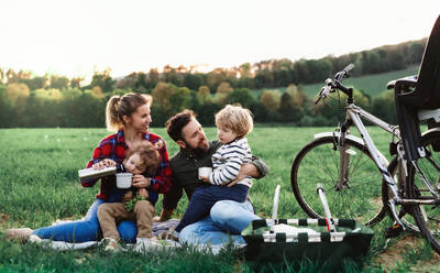 Vorderansicht einer Familie mit zwei kleinen Kindern auf einer Radtour, die im Gras sitzt und sich ausruht. - HPIF13978