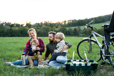 Vorderansicht einer Familie mit zwei kleinen Kindern auf einer Radtour, die im Gras sitzt und sich ausruht. - HPIF13979