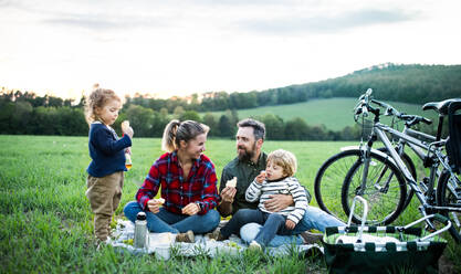 Vorderansicht einer Familie mit zwei kleinen Kindern auf einer Radtour, die im Gras sitzt und sich ausruht. - HPIF13981