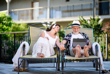 Frontansicht eines älteren Paares mit Tablet und Kopfhörern im Freien im Urlaub, beim Entspannen. - HPIF13989