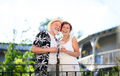 A senior couple holding wine outdoors on holiday, looking at camera. - HPIF13991