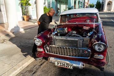 Kubanischer Mann inspiziert und bewundert den offenen Motor eines roten Chevrolet-Klassikers, Cienfuegos, Kuba, Westindien, Karibik, Mittelamerika - RHPLF23922