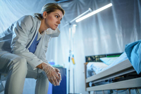 Tired and frustrated doctor sitting by patient in bed in hospital, coronavirus concept. - HPIF14006