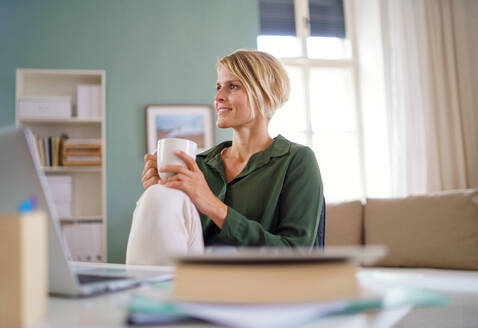 Porträt einer glücklichen Geschäftsfrau in einem Büro, die am Schreibtisch sitzt und eine Tasse Tee in der Hand hält. - HPIF14010