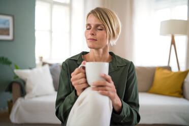 Front view portrait of woman meditating indoors in office, holding cup of tea. - HPIF14011