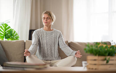 Portrait of woman indoors at home doing yoga, on sofa, mental health and meditation concept. - HPIF14018