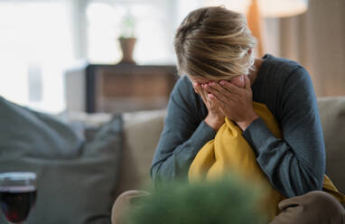 Traurige und gestresste Frau, die zu Hause auf dem Sofa sitzt und weint, Konzept der psychischen Gesundheit und des Coronavirus. - HPIF14028