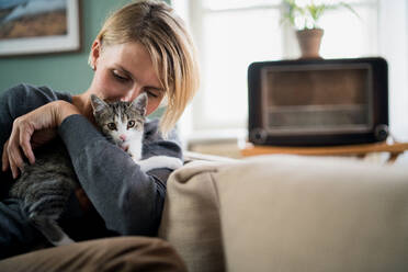 Portrait of happy woman with cat relaxing indoors at home, mental health care concept. - HPIF14035