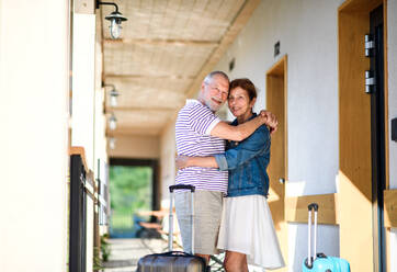 Älteres Paar mit Gepäck, das sich vor der Ferienwohnung umarmt, zurück zum normalen Konzept. - HPIF14077