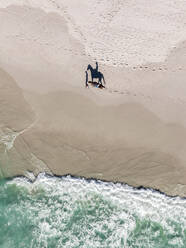 Luftaufnahme einer Person, die auf einem Pferd am Strand entlang reitet, Kapstadt, Südafrika. - AAEF17994