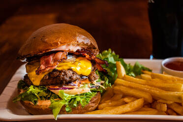 Hausgemachter Cheeseburger mit Käse und Gemüse, serviert mit Pommes Frites und Salat - ADSF44064