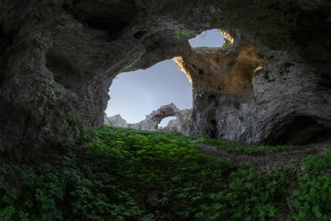 Erdgeschoss der Höhle Arco de Portupekoleze mit Doppelloch in Felsformationen mit grünem Gras in malerischer Landschaft gegen den klaren blauen Himmel in Spanien - ADSF44085