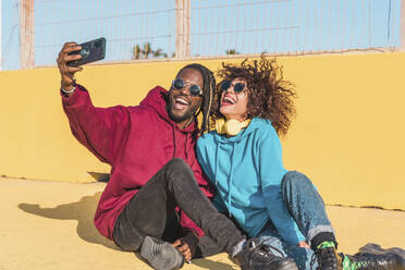 Eine Gruppe von Freunden in bunten Outfits und mit Sonnenbrillen posiert fröhlich für ein Selfie auf einem sonnigen Sportplatz - ADSF44111