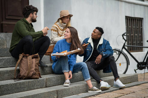 Eine Gruppe fröhlicher junger Leute, die draußen in der Stadt Pizza essen. Coronavirus-Konzept. - HPIF14093
